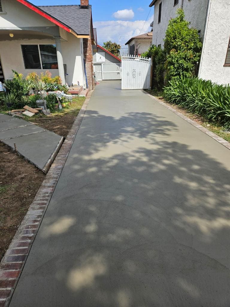 Long concrete driveway with brick border leading to a white gate