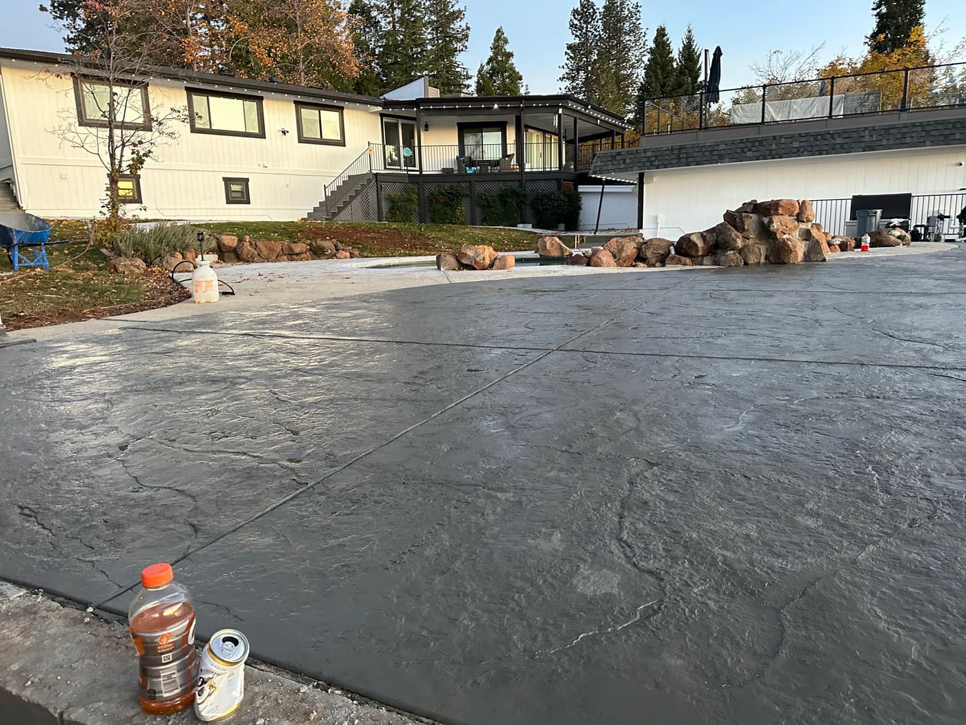 Large stamped concrete driveway and motor court with a boulder-lined backyard beyond