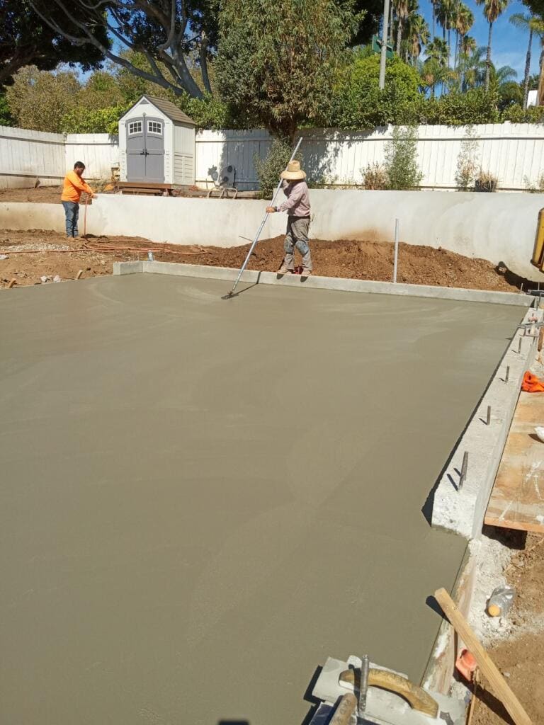 Plain freshly poured concrete driveway slab with a wood fence backdrop