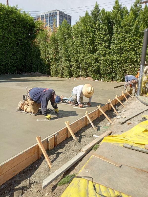 Crew hand finishing the edge of a large concrete foundation slab
