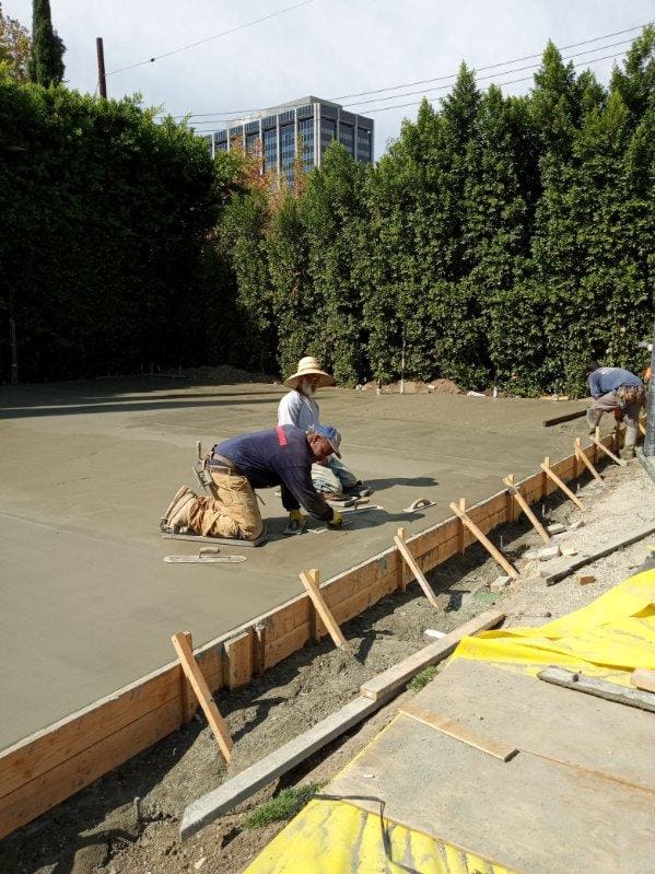 Crew finishing a large concrete slab surrounded by hedges