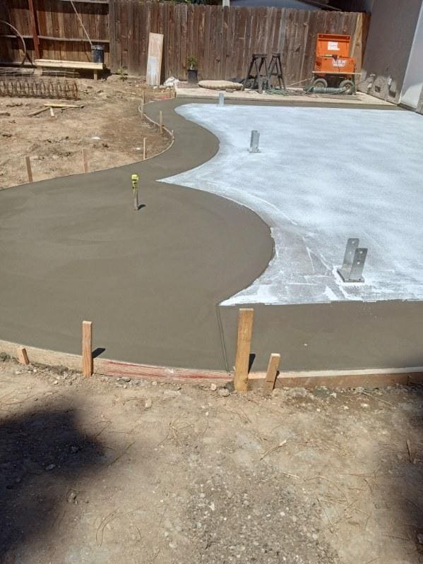 Curved concrete patio slab freshly poured next to a wood fence