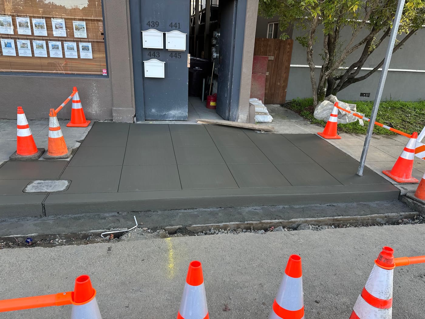 New concrete sidewalk poured at a building entrance with safety cones