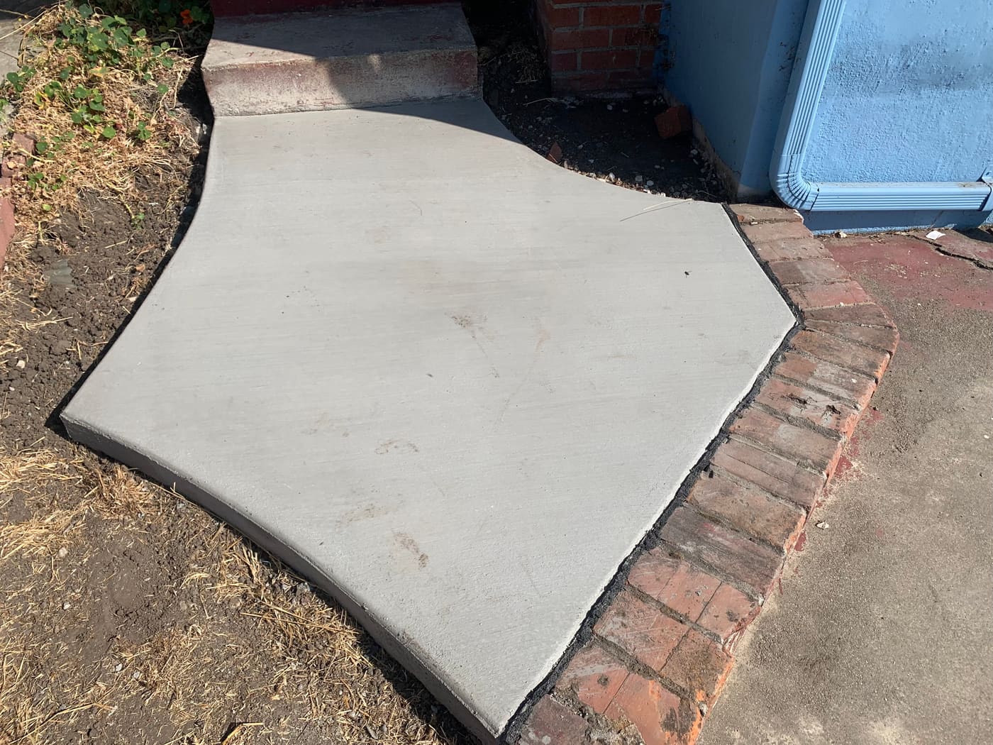 Small curved concrete walkway leading to a side door next to a brick planter